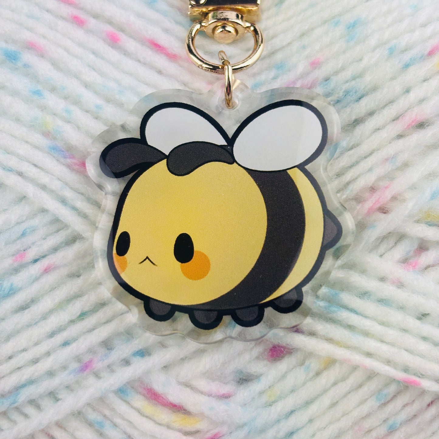 Closeup of a cute bee keychain with a golden clasp with a woollen background.