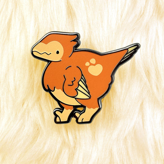 cute dinosaur enamel pin of an orange velociraptor with a yellow details and a loveheart spot. black nickel plating